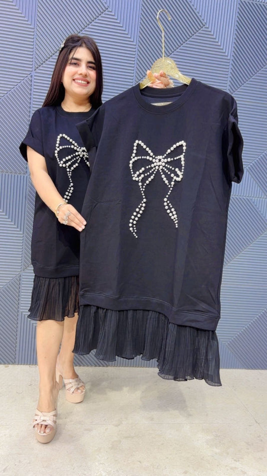 Woman holding a black dress with a bow design against a patterned wall.