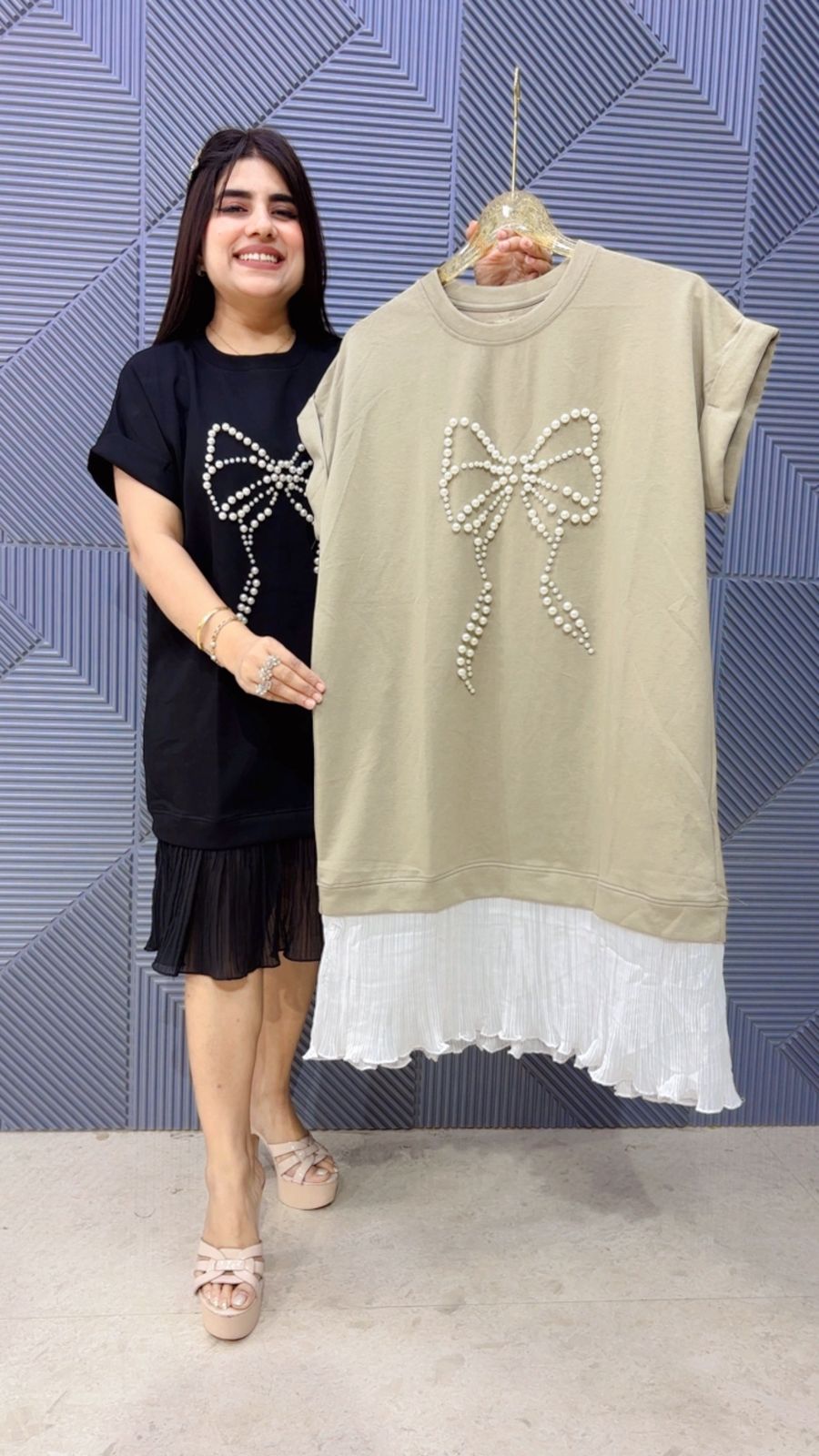 Woman holding a beige dress with a bow design against a blue patterned wall.