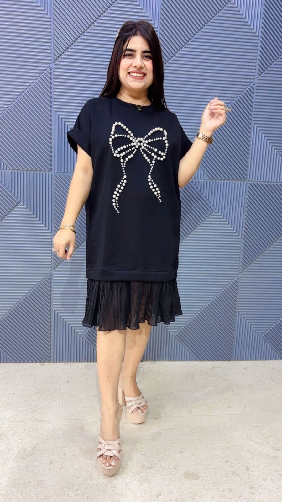 Woman wearing a black dress with a bow design in front of a blue geometric patterned wall.