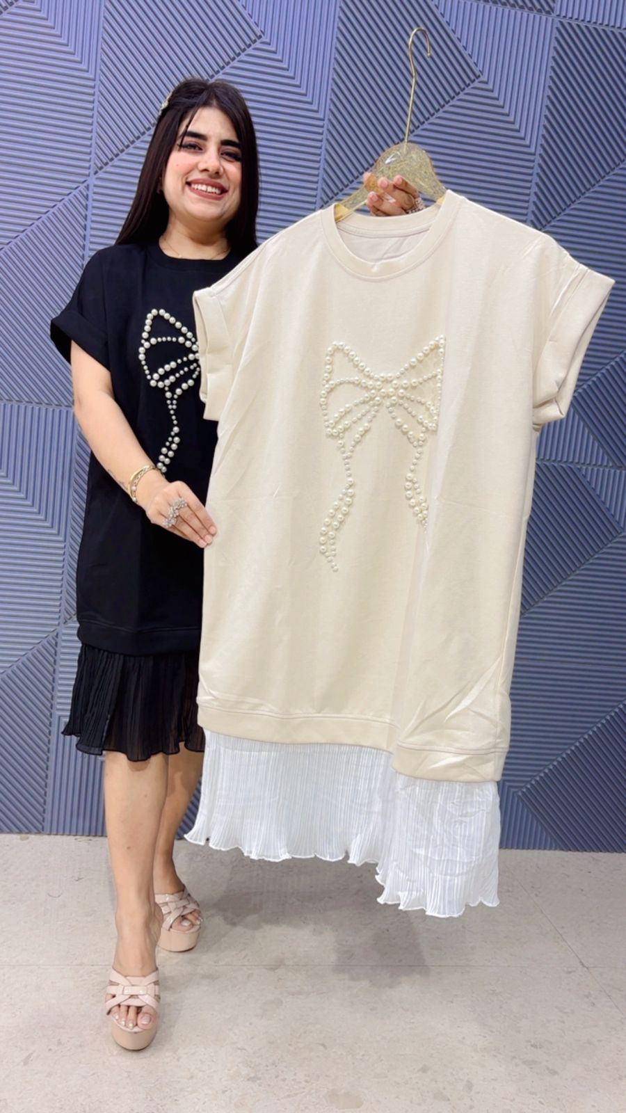 Woman holding a white dress with a decorative bow against a blue patterned wall.